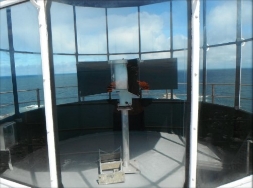 Photograph showing view inside lantern room. Through clear glazing panes, a small beacon is fitted to stand in centre of room. 