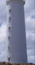 Photograph showing white, rendered lighthouse tower. Six window recesses are set into the tower.