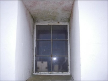 Photograph showing window set deep into tower wall. Clear glazing panes fitted into stainless steel sash and frame. 