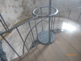 Photograph showing curved room with timber half-floor. A spiral staircase descends from the floor to a lower level. 