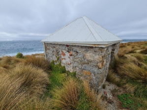 Photograph showing small, rubble stone building sitting amongst grassy vegetation.