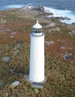 Photograph showing white lighthouse tower in isolated landscape beside blue ocean. 