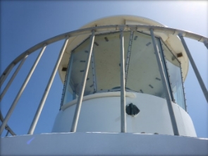 Photograph showing a glazed, white, lighthouse lantern room encircled by railing. 