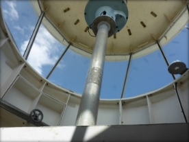 Photograph showing inside of a round lighthouse lantern room with glazing panes fitted. A steel column is fitted with a beacon.  