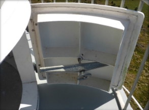 Photograph showing a small door standing ajar, leading out onto a lighthouse balcony. A small handwheel is fitted to the inside of the door. 