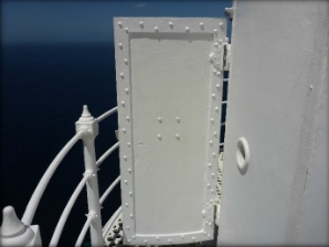 Photograph showing large lantern room door standing ajar, leading out onto lattice balcony.   