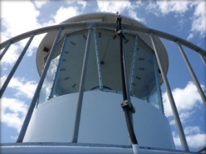 Photograph showing a glazed, white, lighthouse lantern room encircled by railing. 