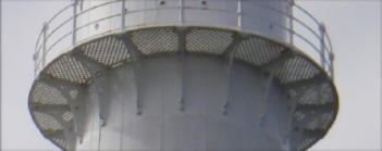 Photograph showing underside of lattice balcony with balustrades wrapping around a white lighthouse tower. 