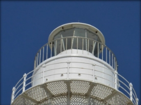 Photograph showing two tiers of white balconies encircling a glazed lighthouse lantern room.  