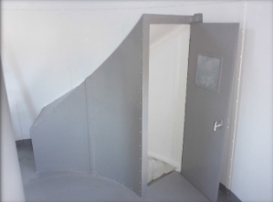 Photograph showing grey airlock enclosure with door standing ajar.  