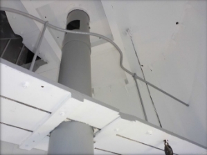 Photograph showing underside of platform fitted around a large weight tube. Underside of floor above can be seen.