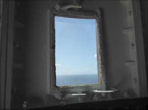 Photograph showing tower window from inside, fitted in cast iron panels. Ocean and sky can be seen through glass. 