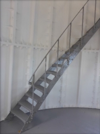 Photograph showing grey staircase fixed to outer edge of curved floor, leading up out of frame. 