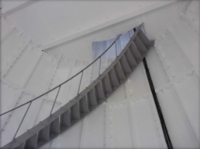 Photograph showing underside of a curved staircase leading to floor above. 