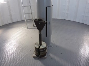 Photograph showing a weight resting beside a grey weight tube fitted to centre of a round, grey floor. 