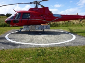 Photograph showing red helicopter resting atop of concrete helipad.