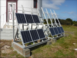 Photograph showing solar panels fixed to frame beside lighthouse tower. 