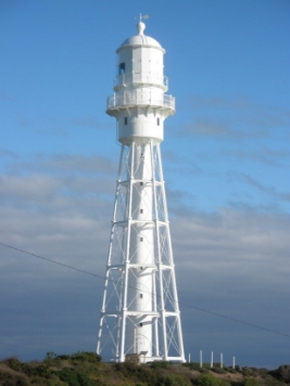 Photograph showing tall, white tower with lattice supports, set against blue sky. 