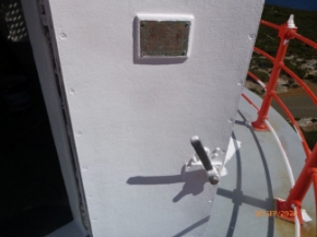 Photograph showing curved lantern house door standing ajar on balcony. Plaque fitted to door.