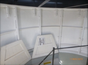 Photograph showing sub-lantern room landing encased in curved cast iron panels. Two floor hatches rest open revealing accessway to floor below. Sign on one hatch reads "Caution Low Headroom"