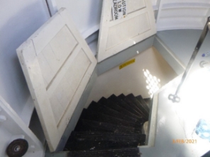 Photograph showing open floor hatch with curved staircase leading down to floor below. 