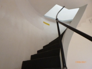 Photograph showing curved staircase leading up to hatch above.