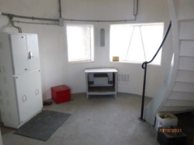 Photograph showing circular room with electrical cabinets and cables. A curved staircase leads from the floor to a level above.