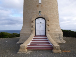 Photograph showing base of stone lighthouse tower with six stone steps leading from ground to front doors. 