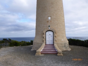 Photograph showing base of stone lighthouse with six steps leading up to front doors. 