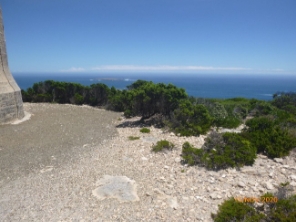 Photograph showing green vegetation beside gravel apron with blue sea and sky behind. 