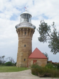 Photograph showing stone lighthouse tower with white lantern house and dome standing beside small annex with red roof. 