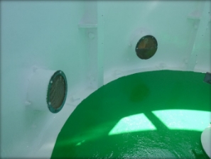 Photograph showing inside of lantern room with circular green floor and curved cast iron panel walls with round vent tubes fitted into panels. 