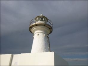 Photograph showing small white lighthouse tower surrounded by solid white fence. 