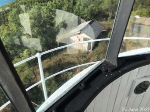 Photograph showing view through clear glazing pane fitted within copper astragals. A shed can be seen on the ground below the tower amongst green vegetation.