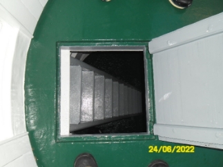 Photograph showing small floor hatch with ladder leading down to floor below. 