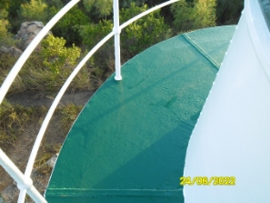 Photograph showing curved balcony floor of lighthouse tower. White railings are fitted to outer edge of floor. 