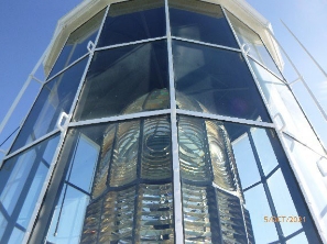 Photograph showing large prismatic lens sitting behind clear glazing panes inside lantern house. 