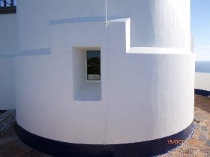 Photograph showing base of white lighthouse tower. A small rectangular window is set into the wall.