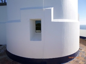 Photograph showing base of white lighthouse tower. A small rectangular window is set into the wall.