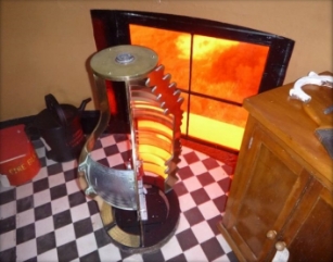 Photograph showing small lens sitting on black and white checker floor beside rectangular window with red glass.