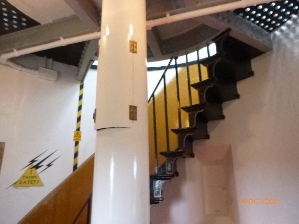 Photograph showing white weight tube fitted to centre of floor, with geometric staircase fitted to curved wall.