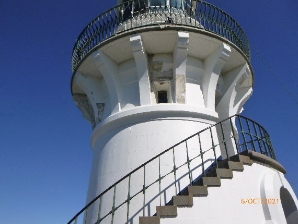 Photograph showing external of white lighthouse tower with external staircase.