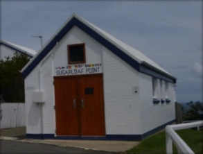 Photograph showing small white brick building with large wooden double doors above which reads "Sugarloaf Point".