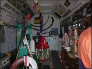 Photograph showing internal of small white building. The internal walls are covered in historic memorabilia, and various artefacts on display.